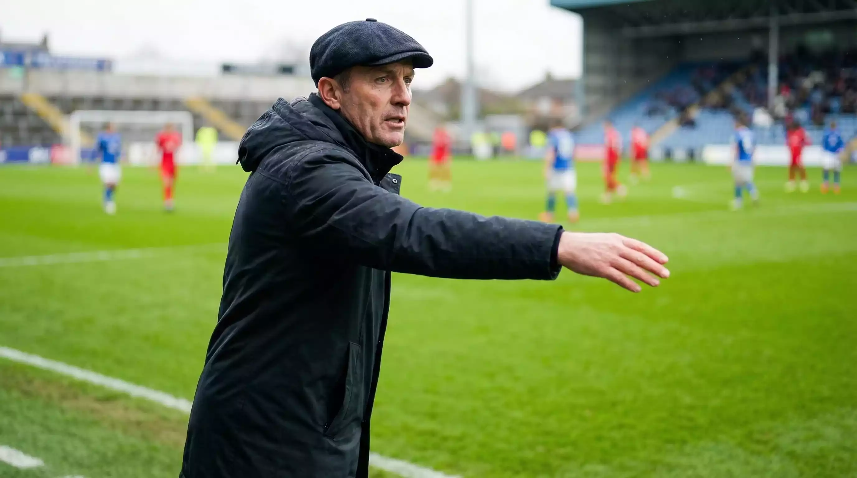 Fodboldtræner peger mod banen ved sidelinjen under en kamp