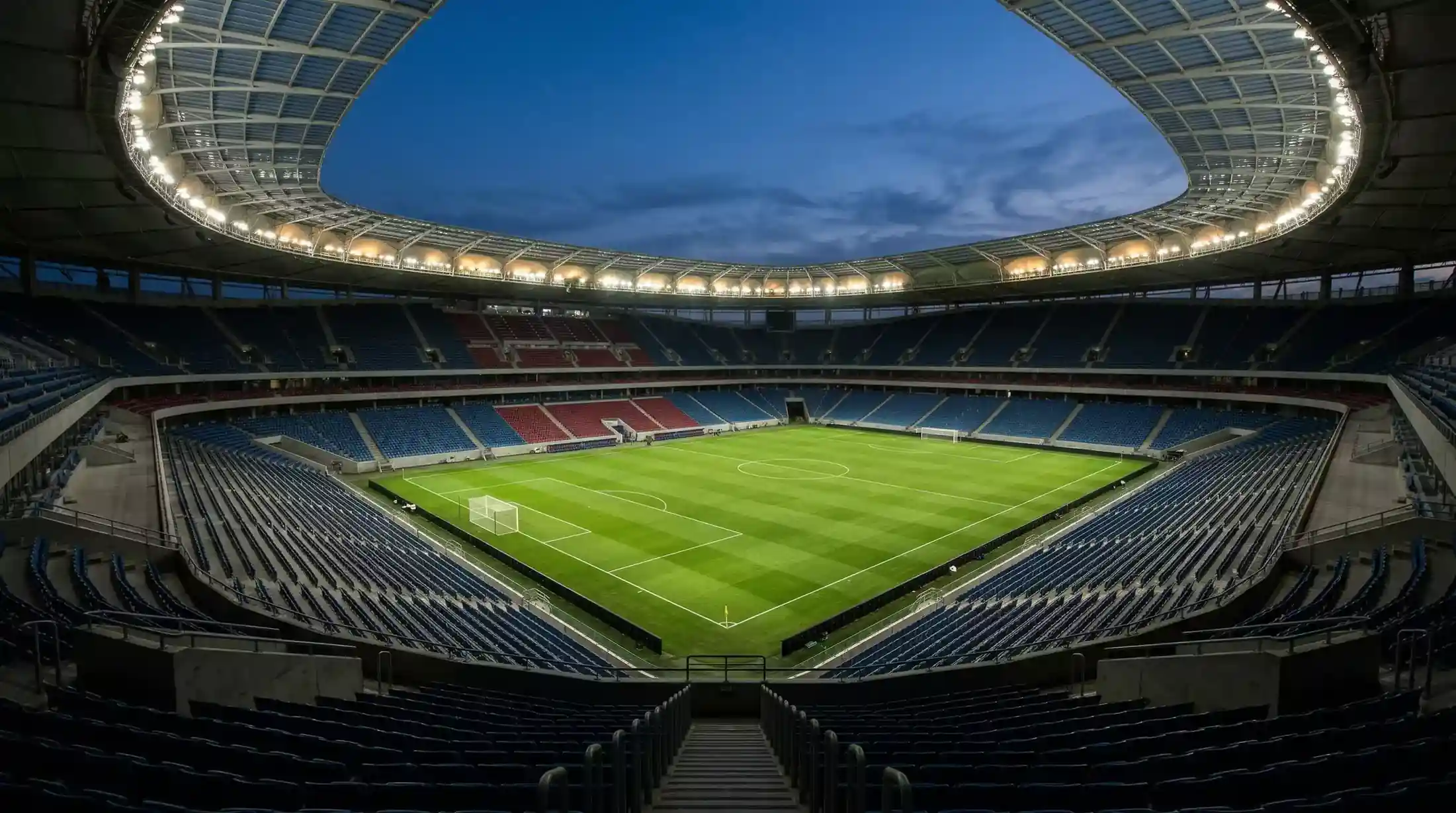 Oplyst fodboldstadion om aftenen med tomme tribuner og grøn græsbane